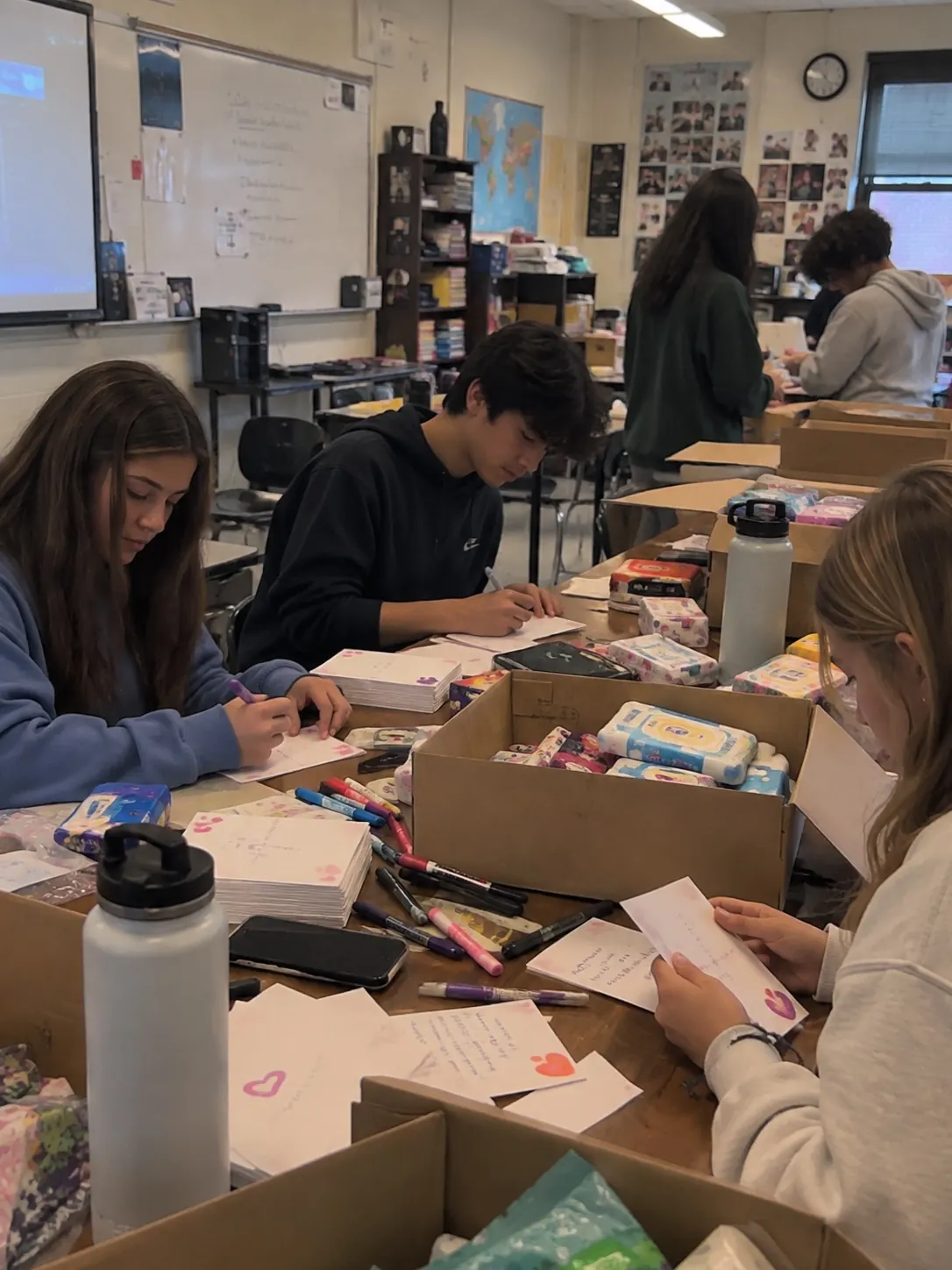 Detailing for MCAS volunteers handwriting inspiration cards for patients at a classroom table