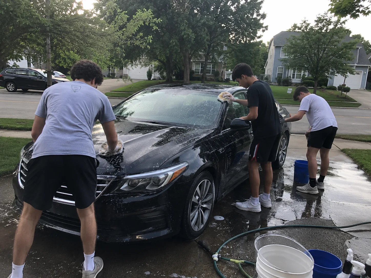 Three Young Detailers volunteers washing a car in a driveway at a fundraising event